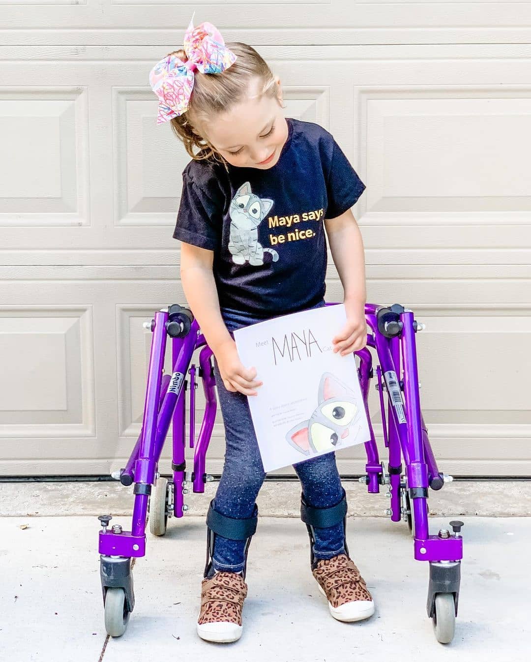 Girl with cerebral palsy holding Meet Maya Cat inclusive children's book, wearing Maya shirt