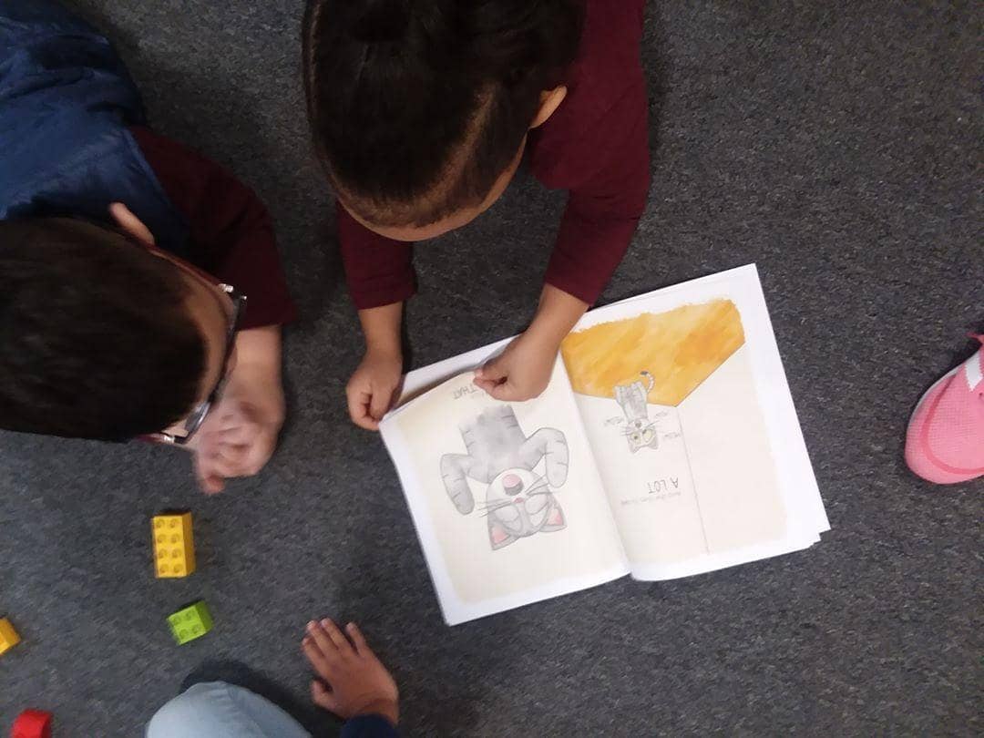 Children read Meet Maya cat book on floor